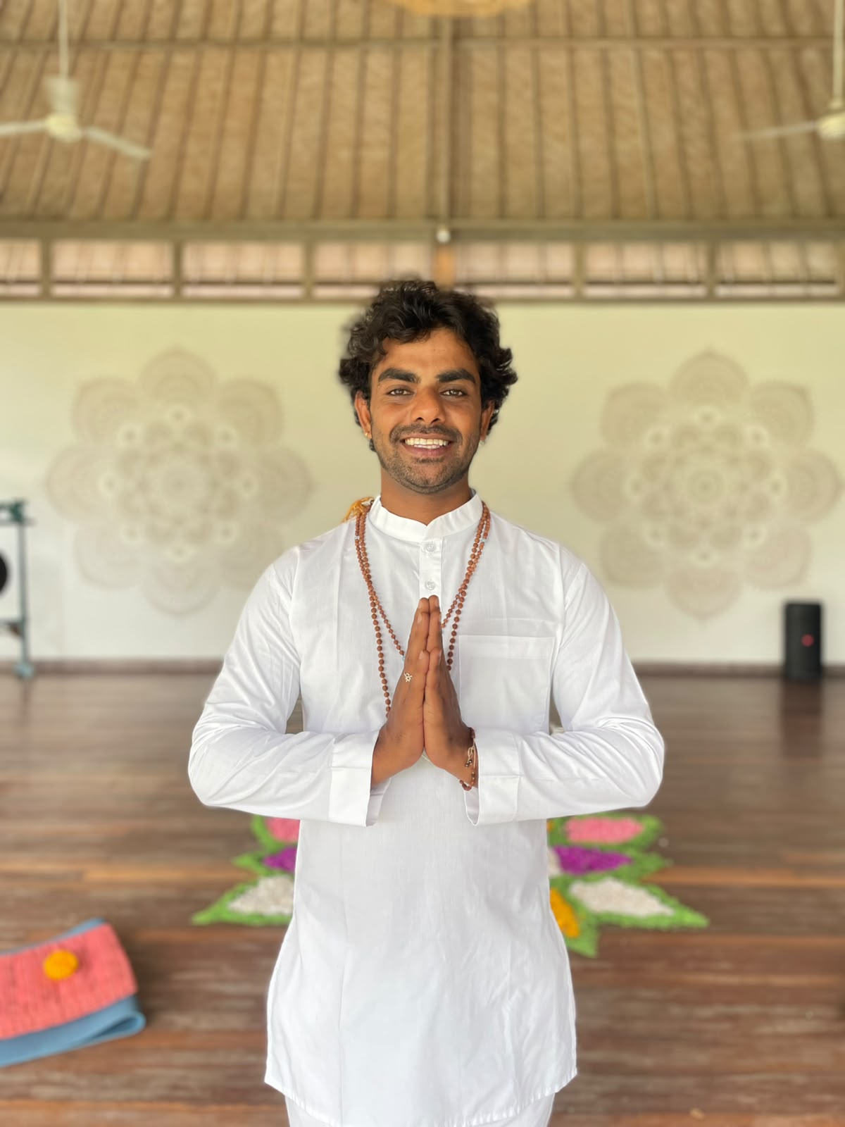 Navin, Taru Yoga teacher, standing in namaste posture inside a yoga shala